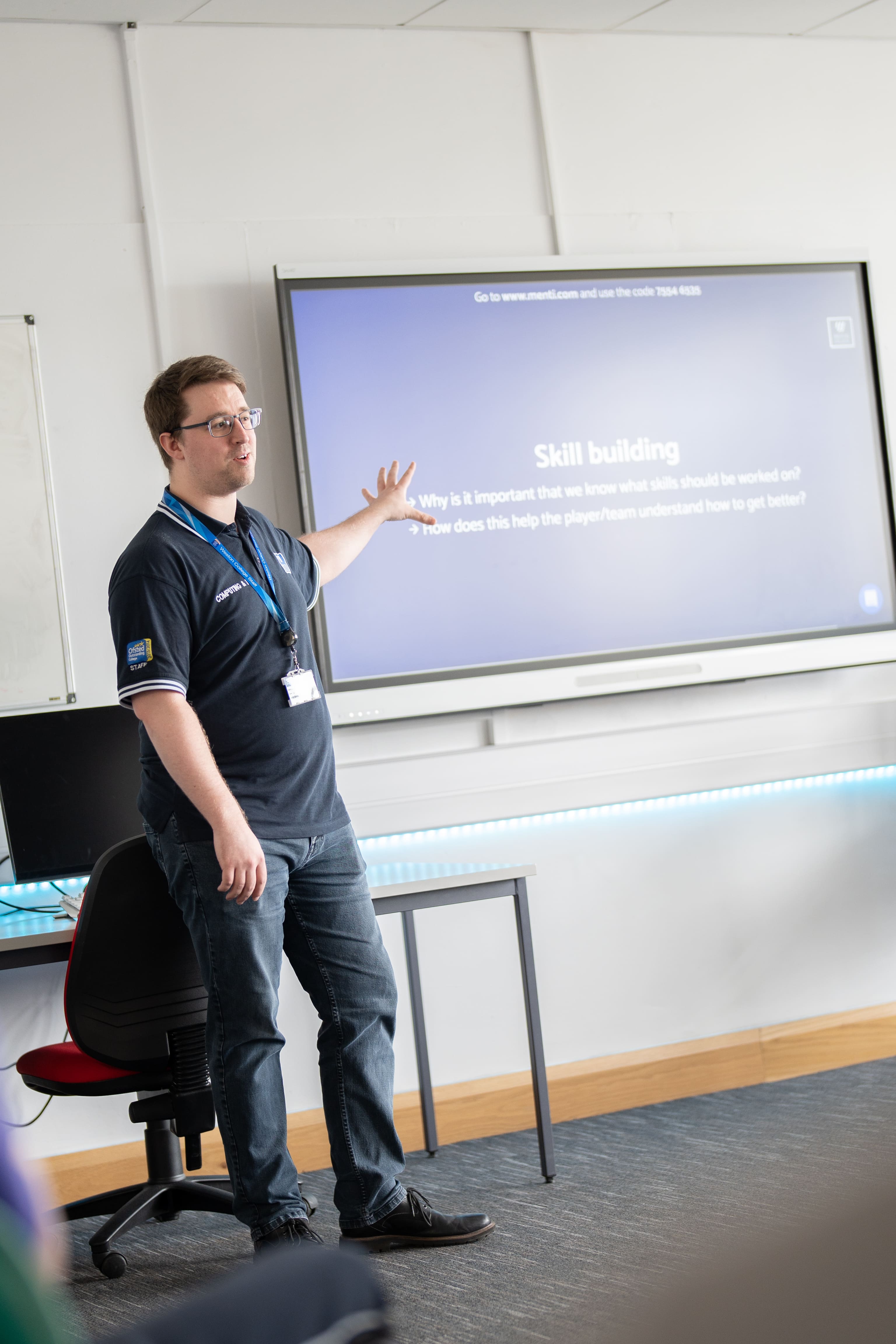 lecturer at the front of a classroom pointing to an interactive whiteboard