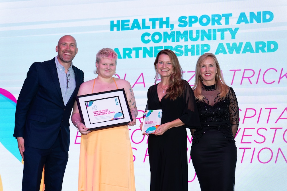 Lola, standing on stage with her employer, Jaqui Ford and Joe Simms accepting her award