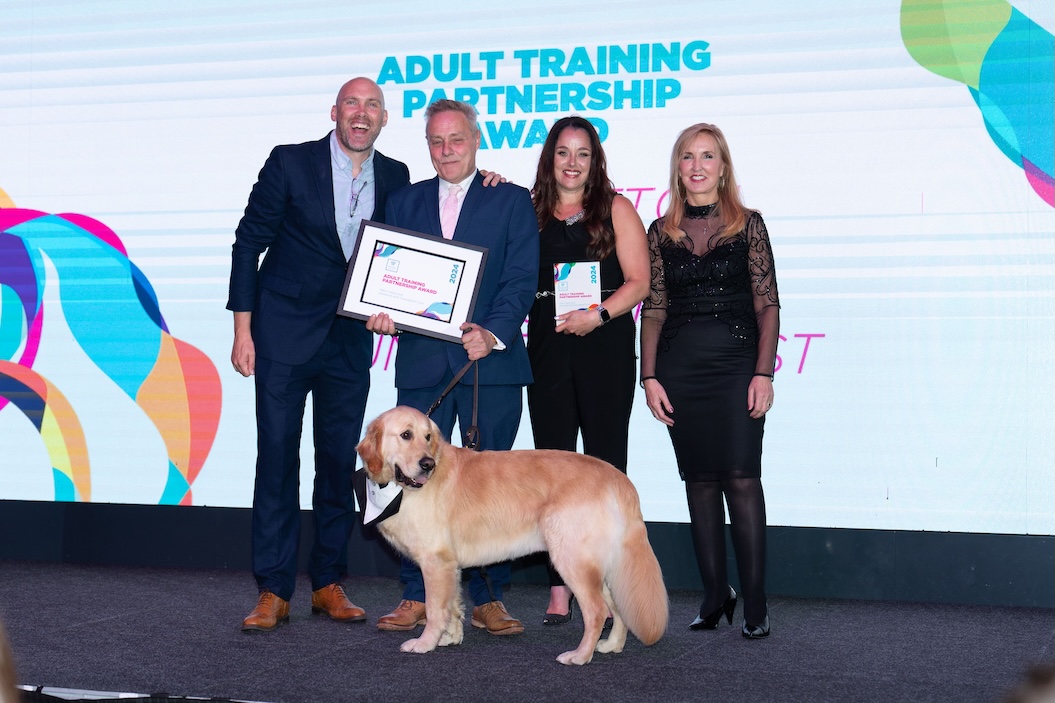 Mark, standing on stage with his employer, guide dog, Jaqui Ford and Joe Simms accepting his award