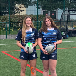 lottie and katie standing mnect to eachother holding rugby balls