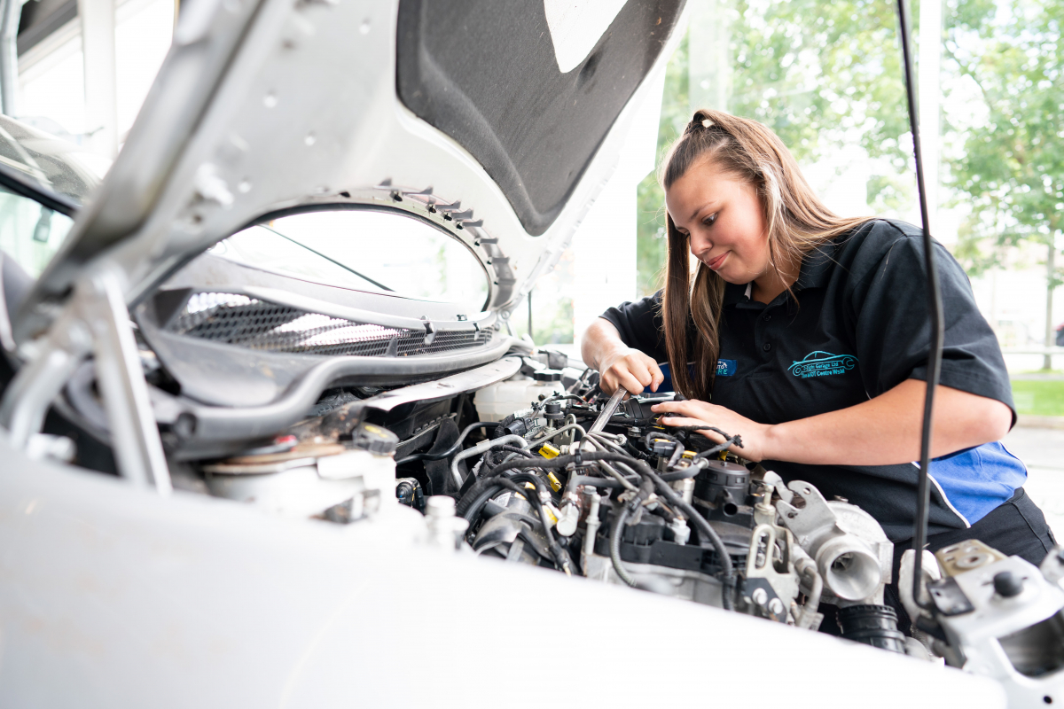 a girl concentrates while she works under the bonnet of a car