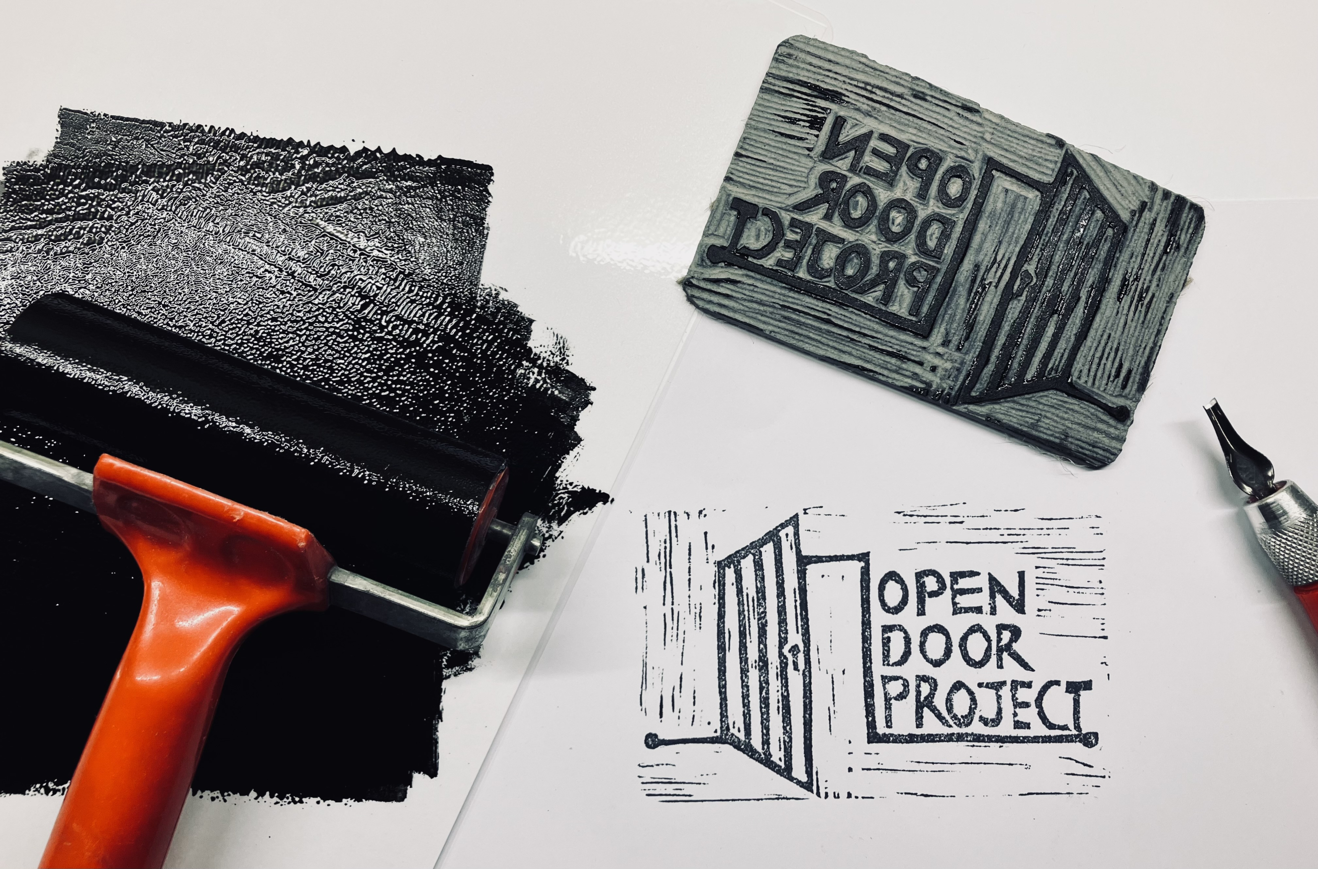 Painting a wall black using a roller, with the words 'Open Door Project' on the side