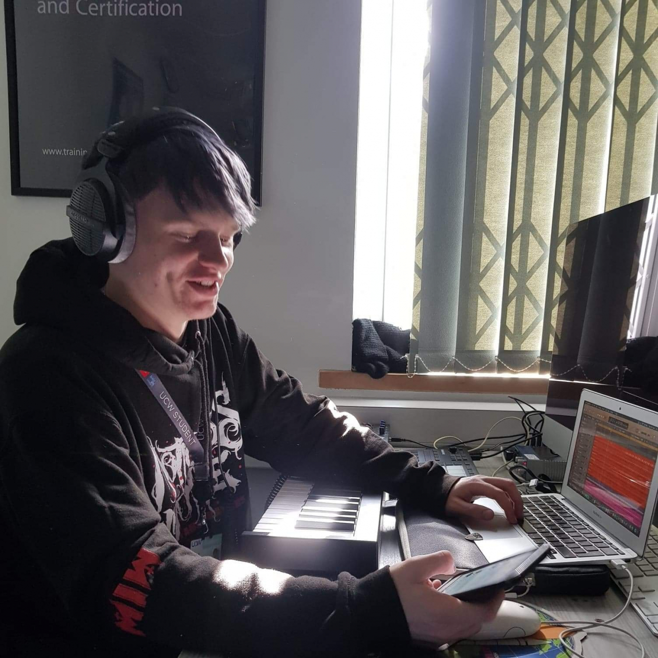 Male student holding phone and laptop with headphones on