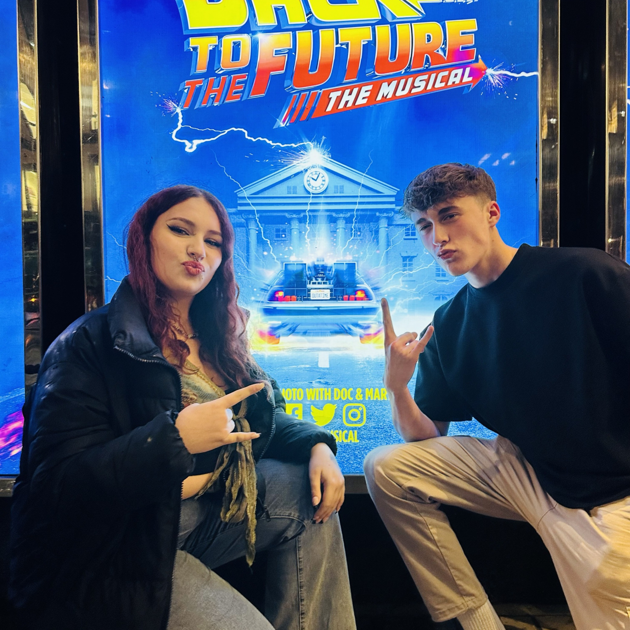 a female and male student posing in front of the back to the future musical poster in London