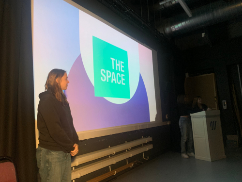 3 students standing next to their charity presentation, The Space