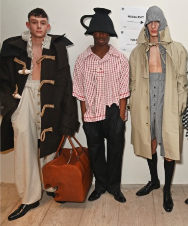 Three of William's designs on models: 1 in a large, oversized duffle coat, 1 tea towel flannel shirt and a teacup hat, and 1 in a brown coat and a hoodie jumpsuit