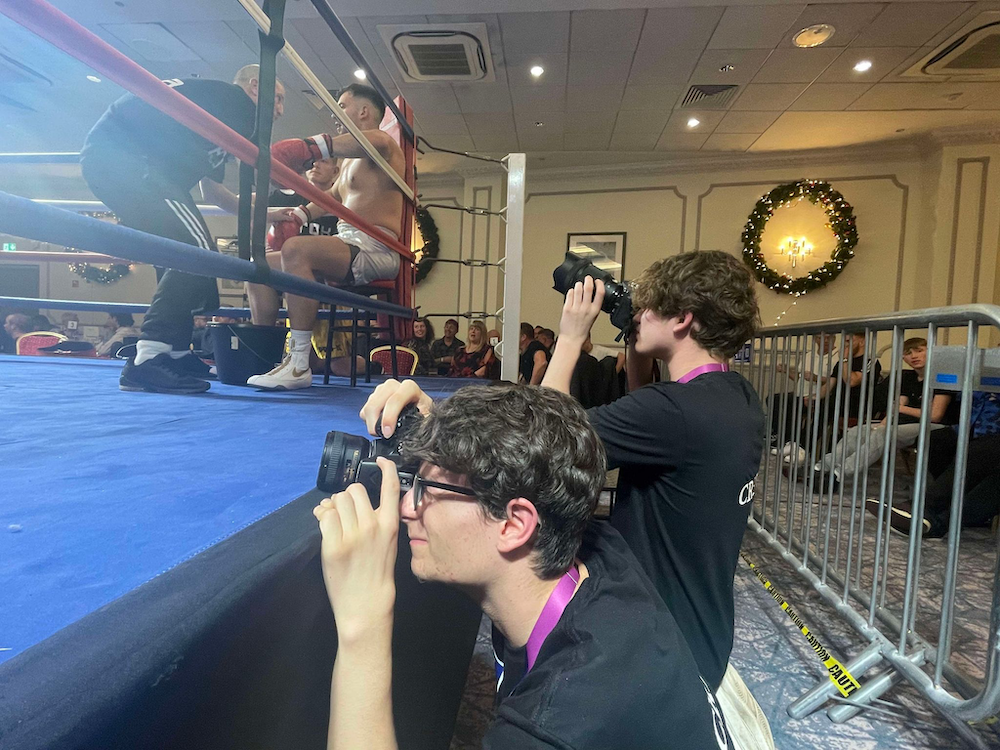 2 students taking pictures ringside of a boxing match