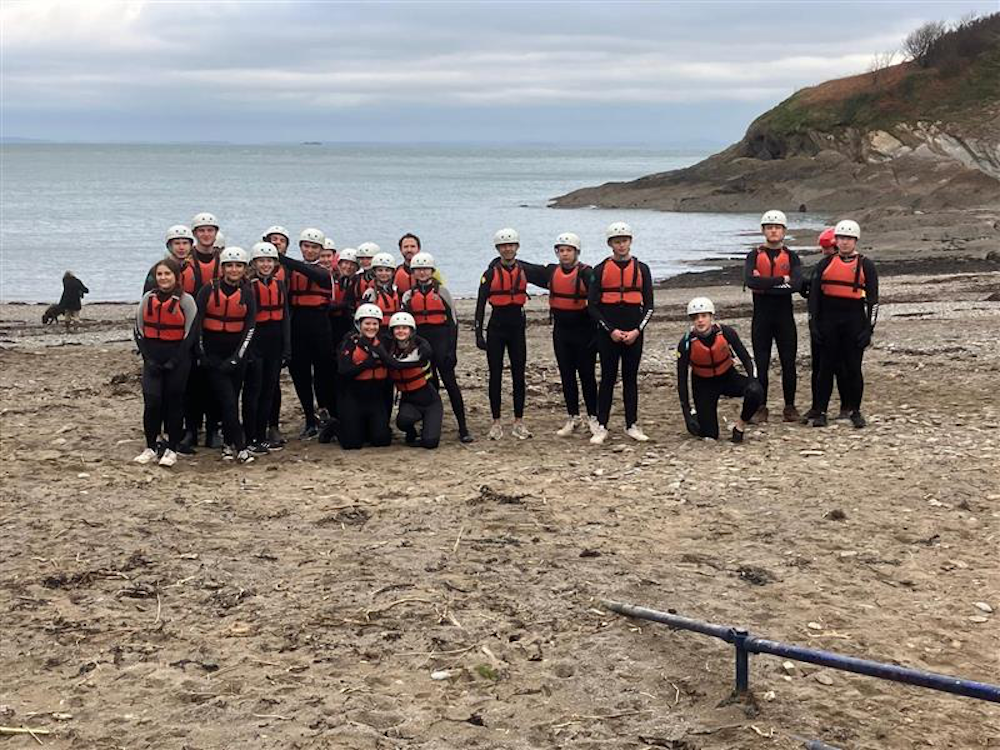 a group of students standingon a beach with helmets and life jackets on