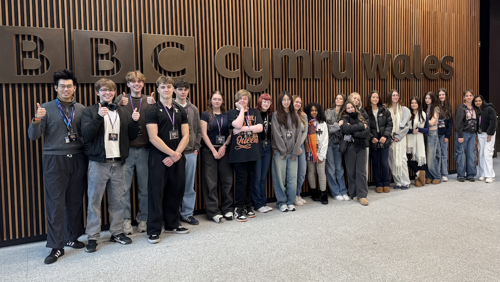 Students standing infront a a big BBC Cymru Wales sign at BBC Cymru Wales studios.